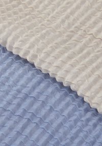 Tekstureret stof i creme og lyseblå med et bølget mønster. Det cremefarvede materiale overlapper det blå og skaber en lagdelt effekt.