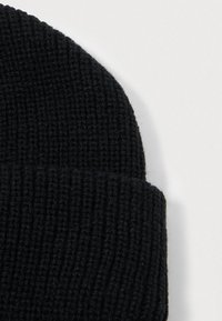 Čierny pletený čiapka s vertikálnou rebrovanou textúrou a ohnutým okrajom pre zvýšené teplo a tesné priliehanie.