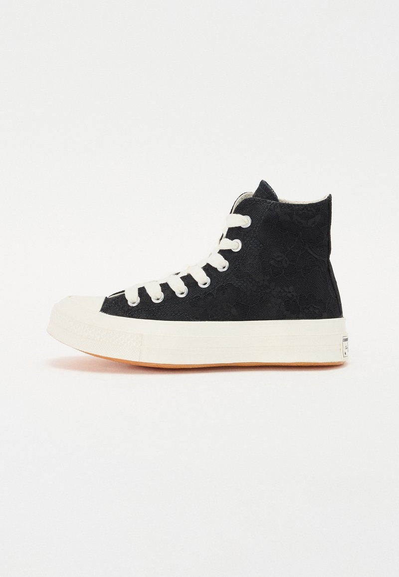 Zapatilla alta negra con diseño de cordones, ojales y cordones en blanco. Punta de goma y suela de goma. Acentuada con un patrón texturizado.
