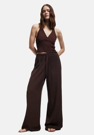 Top corto marrone con scollatura a halter, texture arricciata e bordi volant, abbinato a pantaloni della tuta marroni larghi con vita elasticizzata.