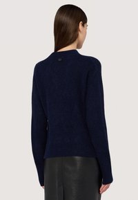 Marinblå stickad tröja med ett strukturerat diamantmönster, rund halsringning och en liten logotypmärke baktill. Långa ärmar och ribbad nederkant.