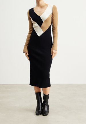 Woman wearing a midi black dress with beige and white geometric pattern on the upper part and black ankle boots.