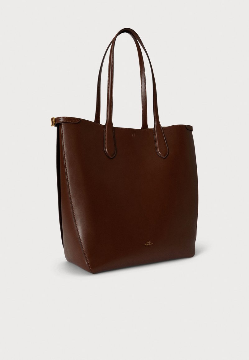 Braune Ledertasche tote mit zwei langen Griffen. Glatte Textur, offenes Oberteil, mit dezentem Gold-Branding vorne.