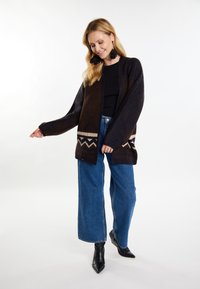 Cardigan maron și albastru cu un model geometric, cu deschidere frontală și mâneci largi, asortat cu blugi cu talie înaltă și cizme negre până la gleznă.