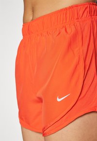 Shorts de sport orange avec une texture en mesh, ceinture élastique et logo Nike blanc sur le bas à gauche.