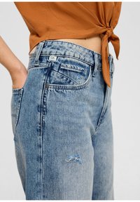 Ljusblå jeans i denim med en avslappnad passform, med slitna knän, framfickor och en märkt etikett på midjebandet.