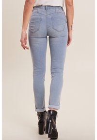 Jean skinny bleu clair avec taille haute, dotés de deux poches arrière, d'un ourlet roulé, portés avec des bottines à talons noirs.