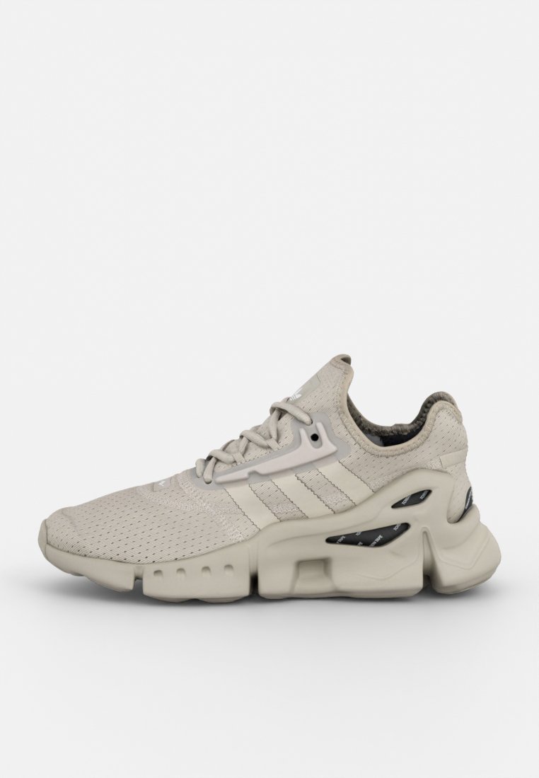 Zapatilla deportiva beige con parte superior de malla, tres franjas laterales, suela acolchada y cortes distintivos en la entresuela para transpirabilidad.