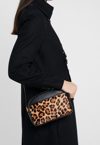Kabelka s leopardím vzorem a texturovaným černým vrškem. Kulatý tvar, dvojí materiály a odnímatelný popruh. Nosená po boku k černému kabátu.