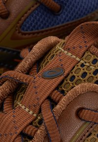 Bruna och blåa sportskor har en ovandel i mesh, texturerade skosnören och en framträdande logodetalj, med kontrasterande sömmar och detaljer.