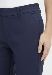 Navy blue trousers with a smooth texture, featuring front pleats, a side pocket, and a straight cut. The waistband has a subtle design.
