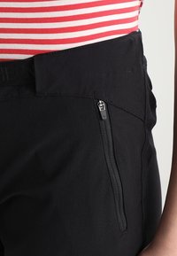 Black pants with a partially visible zippered pocket and smooth texture. Features a wide waistband. Background shows a striped top.