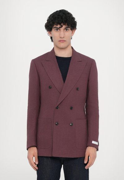 Blazer burdeos de doble botonadura en tejido texturizado, con botones negros, solapas de muesca y dos bolsillos frontales, usado sobre una camisa negra.