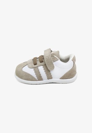 Zapatilla beige y blanca para niño pequeño con detalles en ante, dos tiras de velcro y suela de goma blanca, mostrada de lado sobre un fondo blanco.