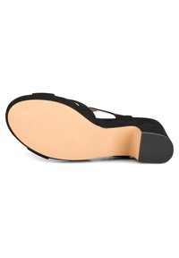 Zapato de tacón alto de ante negro con suela de goma en tono marrón claro. Presenta un diseño de punta abierta y tiras entrecruzadas. Base de tacón plana para estabilidad.