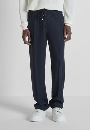 Pantalones azul marino oscuro con cordón, combinados con zapatillas blancas y un suéter blanco de manga larga con textura.