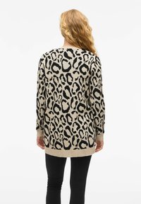 Jersey de manga larga beige con un patrón de leopardo negro. Presenta un cuello redondo y puños y dobladillo acanalados. Se lleva con pantalones negros ajustados.