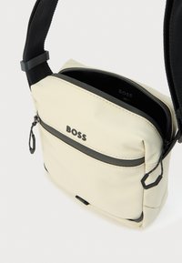 Kreemivärvi üheõlaline kott musta tõmbluku ja detailidega, valmistatud tekstureeritud kangast. Omab silmatorkavat logo ja reguleeritavat rihma.