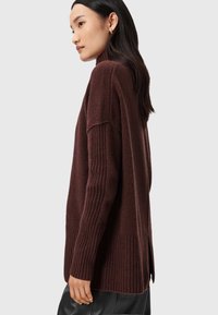 Bordeaux striktrøje med høj hals, ribbede ærmer og sideslids. Den bløde tekstur og den afslappede pasform øger komforten.