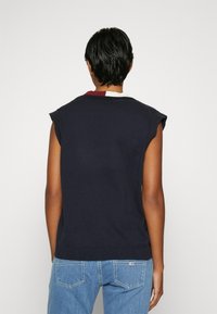 Marineblauer ärmelloser Pullover aus weichem Material, mit Rundhalsausschnitt und geripptem Saum. Die Rückseite zeigt ein Farbblockdesign mit kastanienbraunen Akzenten.