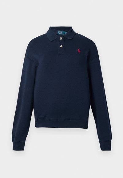 Temno modra polo majica z dolgimi rokavi, z dvema gumboma, valovitimi manšetami in robom, ter majhnim rdečim izvezenim logotipom na levem prsnem delu.