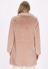 Palton din blană sintetică de culoare bej deschis, cu guler tip șal, mâneci lungi și o croială lejeră. Textură netedă, cu un design până la genunchi.