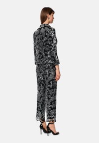 Black and silver sequined suit with a structured blazer and wide-leg pants. High-heeled black sandals complete the outfit.
