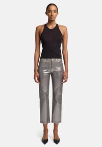 Zwarte mouwloze top gecombineerd met metallic zilveren rechte broek. De broek heeft een subtiele glans en een cropped lengte, geaccentueerd door zwarte hakken.