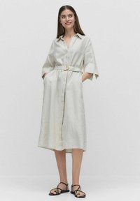 Jasnokolorowa lniana sukienka koszulowa z przednim zapięciem na guziki, krótkimi rękawami i paskiem w talii z okrągłą złotą klamrą.