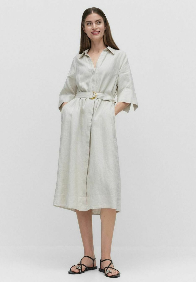 Jasnokolorowa lniana sukienka koszulowa z przednim zapięciem na guziki, krótkimi rękawami i paskiem w talii z okrągłą złotą klamrą.