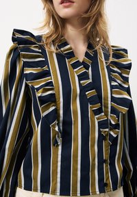 Blouse rayée bleu marine et olive avec des accents froncés, décolleté en V et fermeture à bouton, fabriquée en tissu léger.