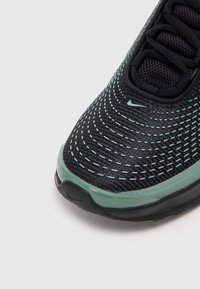 Crne atletske cipele s teksturiranim pletenim gornjištem, akcentima u boji mente i podstavljenim ovratnikom. Imaju zakriveni potplat i minimalistički Nike logo.