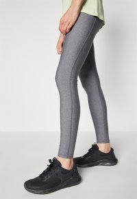 Harmaat leggingit, joissa on sileä pinta ja tiukka muotoilu, yhdistettynä mustiin urheilukenkiin, joissa on verkko- ja kumikoristeita.