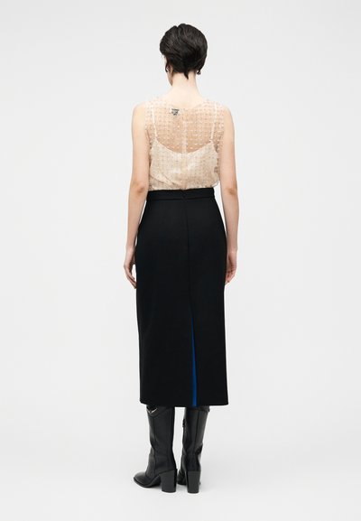 Top bege transparente sem mangas com enfeites texturizados, combinado com uma saia midi preta com uma fenda lateral azul e botas pretas até ao joelho.