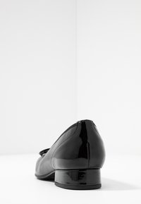 Black leather low-heeled shoe with a patent finish, rounded toe, and a subtle seam detail. Smooth texture with a glossy accent.