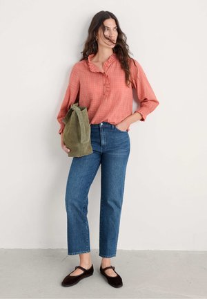 Light coral long-sleeve shirt with ruffled collar, blue high-waisted jeans, and dark brown Mary Jane shoes; holding a green suede bag.