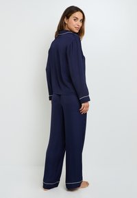 Ensemble de pyjama bleu marine en tissu léger, comprenant des manches longues, un pantalon large et un piping blanc contrastant le long des bords.
