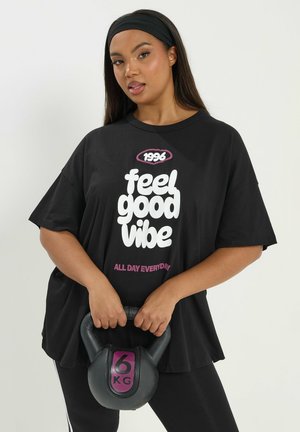 Donna che indossa una maglietta nera con la scritta "feel good vibe" e una fascia per capelli, che tiene in mano un kettlebell da 6 kg davanti a uno sfondo bianco.