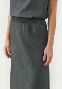 Donkergrijze, gestructureerde rok met een elastische tailleband. De stof heeft een geplooid uiterlijk, wat een subtiele, gelaagde uitstraling creëert.