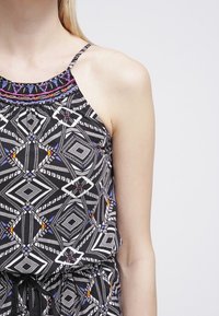 Top con estampados en blanco y negro que presenta diseños geométricos, acentos coloridos y un escote con cuentas y tirantes finos. El material parece ligero.