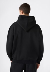 Sudadera negra hecha de tela suave con una gran capucha puntiaguda. Presenta hombros caídos y puños acanalados, con un ajuste holgado.