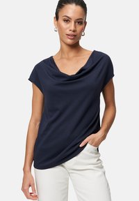 Navy blue cowl neck top with short sleeves, featuring a relaxed fit and soft texture, paired with light-colored trousers.