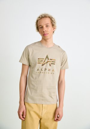 Beige Baumwoll-T-Shirt mit einem Camouflage-Logodesign und gestreiften Akzenten, rundem Ausschnitt und kurzen Ärmeln, kombiniert mit gelben Hosen.