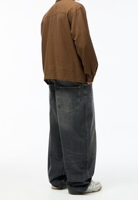 Camisa de manga larga con cuadros marrones combinada con jeans gris oscuro de corte suelto. Los zapatos son de color gris claro con un diseño sutil.