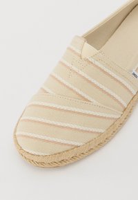 Espadrille en toile beige avec des rayures rose clair et blanches, bout rond et semelle en jute tissée. Texture lisse et design simple.