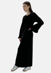 Robe longue noire à coupe décontractée, avec des manches longues et un col rond. Associée à des baskets blanches pour contraster avec le tissu sombre.