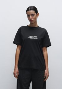 Sort bomulds t-shirt med korte ærmer og afslappet pasform, med hvid tekst der står "LITTLE MISS UNDERSTOOD" henover brystet.