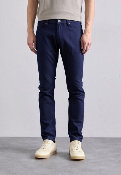 Donker marineblauwe spijkerbroek met een slim fit, vijf zakken, metalen knoopsluiting en subtiele stikseldetails op de zakken.