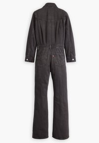 Juoda džinsinė kombinezonas su ilgomis rankovėmis, apykakle ir dviem galinėmis kišenėmis. Pasižymi mygtukų užsegimu ir tiesiais kelnių sijonais.