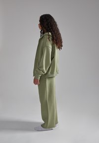 Felpa verde oliva e pantaloni abbinati realizzati in materiale morbido. Il cappuccio oversize presenta una grande tasca e maniche larghe.